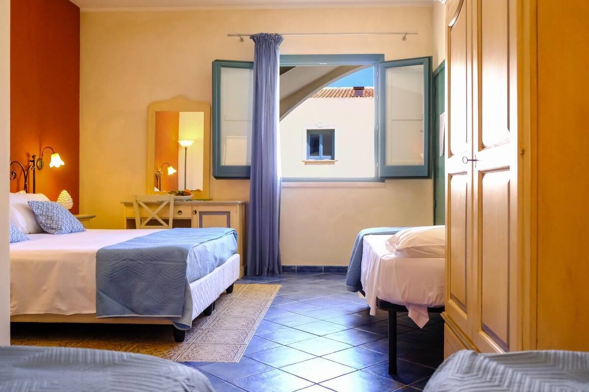 A hotel room with two beds, a desk, a chair, a window with a view, and a mirror.