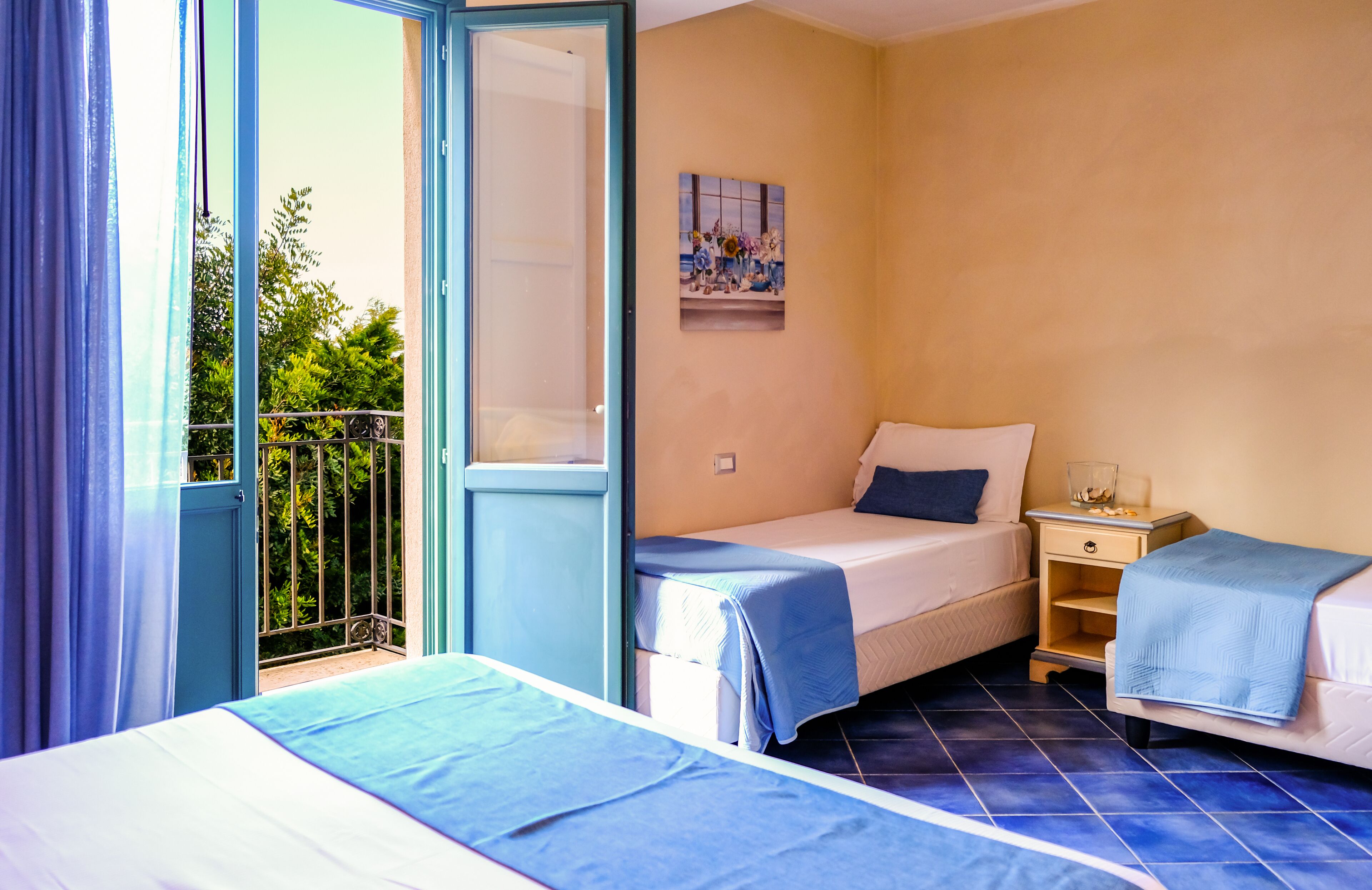 Een hotelkamer met twee bedden, een tafeltje, een nachtkastje en een raam met uitzicht op groen.