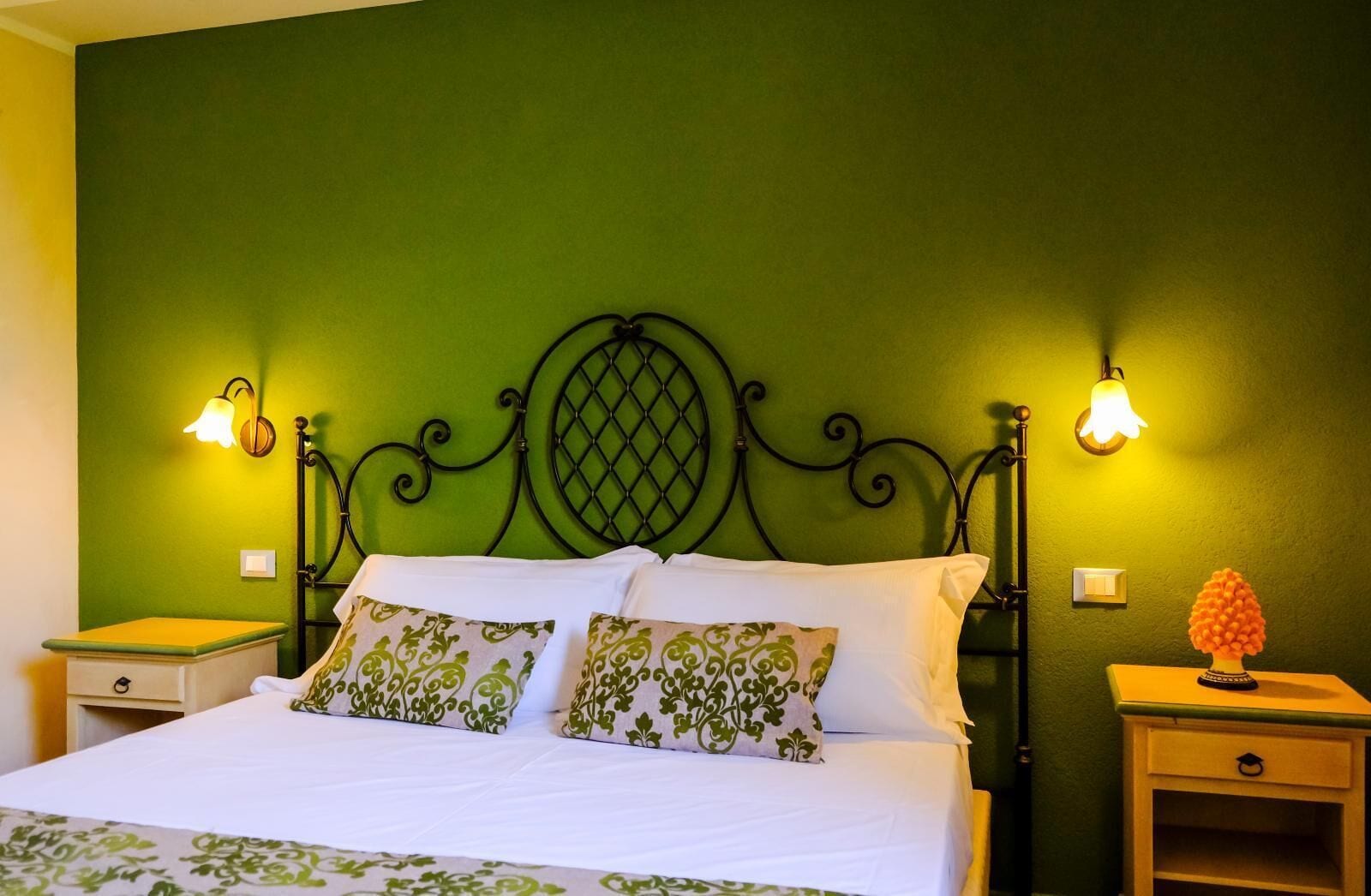 A bed with a green headboard, two bedside tables, and two wall-mounted lamps.