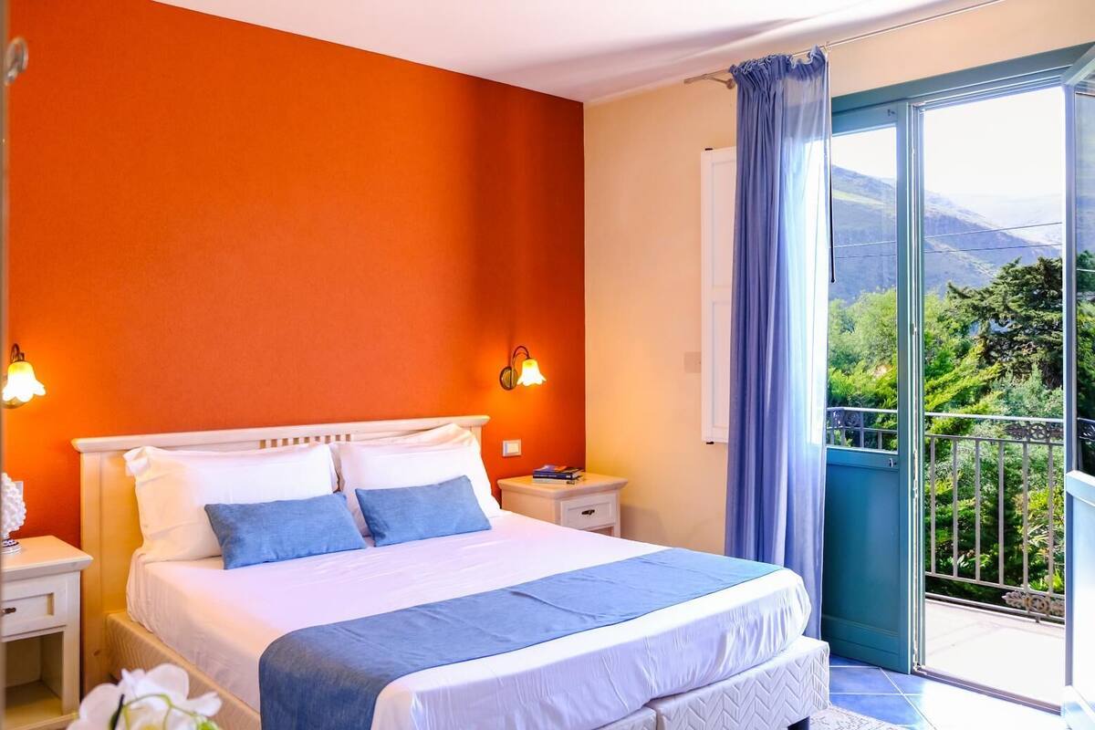 A hotel room with a large bed, two bedside lamps, a nightstand, and a view of a balcony with a railing.