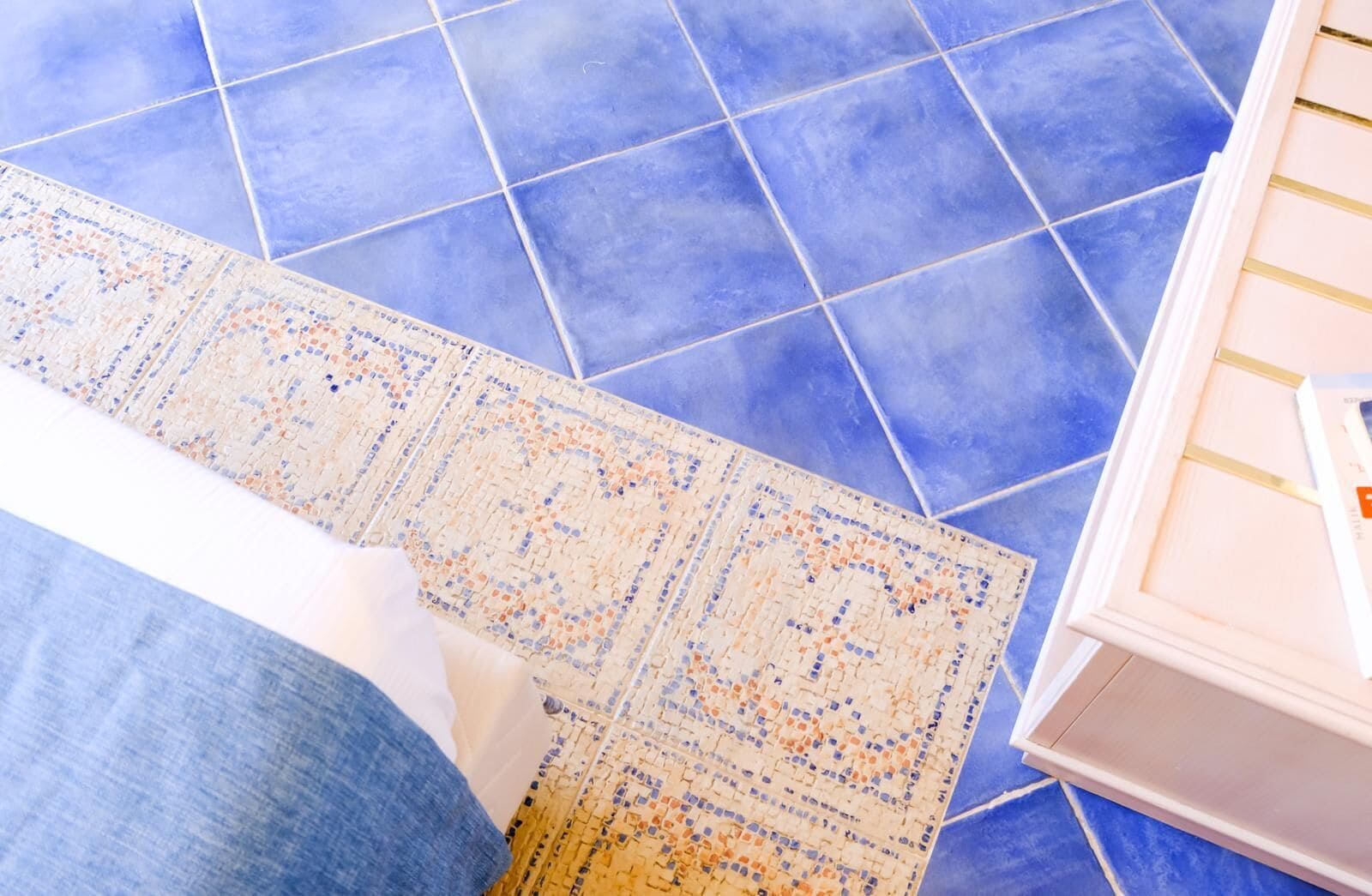 A room with blue tiled flooring, a patterned rug, and a white cabinet.