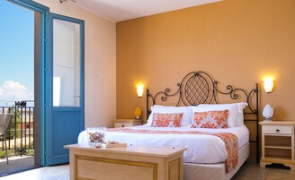 Ein Schlafzimmer mit Bett, Nachttischen, einem kleinen Tisch, einer Glasvase mit Muscheln und einem Balkon mit Aussicht.