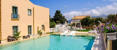 A swimming pool with lounge chairs and a building with balconies.