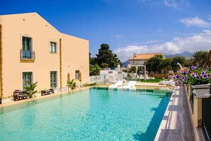 A swimming pool with lounge chairs and a building with balconies. - Hotel Baglio di Scopello (Castellammare del Golfo)