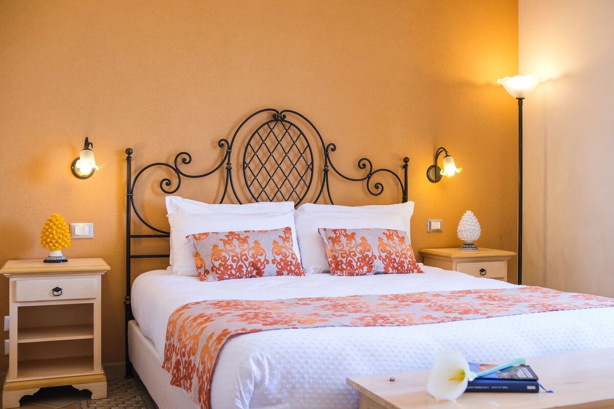 A neatly made bed with a floral-patterned bedspread, two matching pillows, and a nightstand with a lamp and a pineapple-shaped decoration.