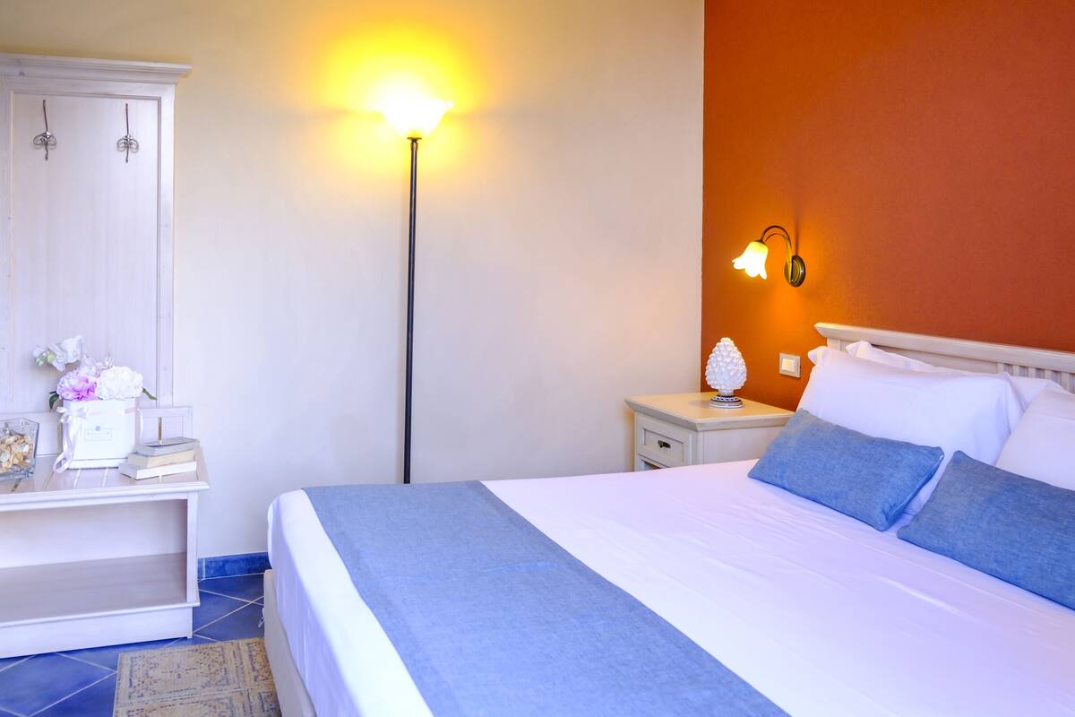 A neatly made bed with a blue accent, a white nightstand with a lamp, and a white wardrobe.