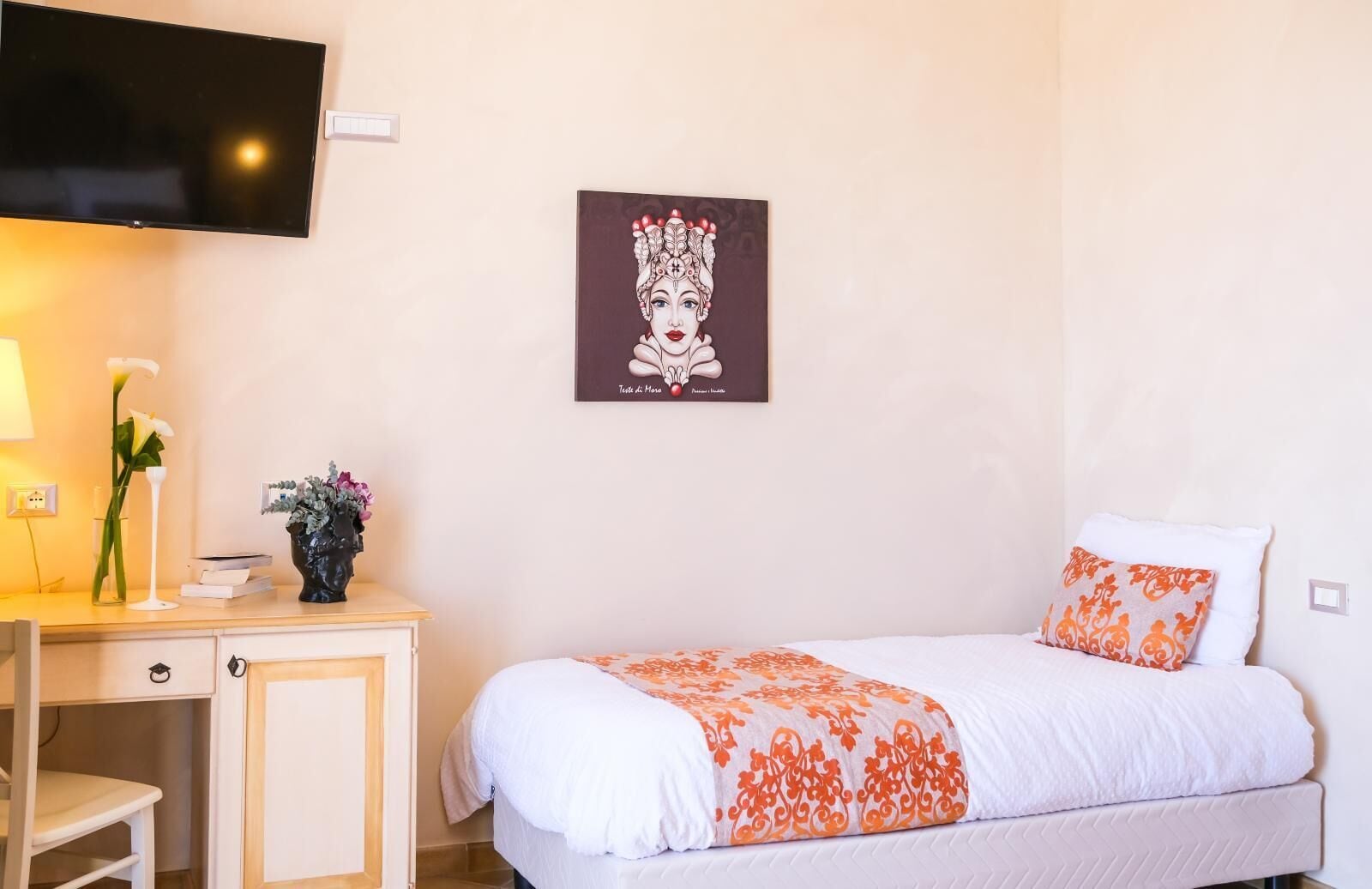 A hotel room with a bed, a desk, a TV, and a framed artwork on the wall.
