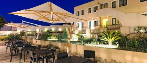 An outdoor patio with tables and chairs, umbrellas, and a building with balconies.