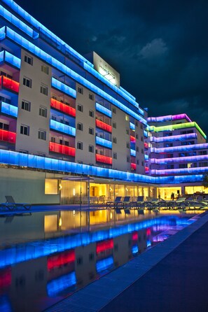 A multi-story hotel with balconies illuminated in various colors, a pool area with lounge chairs, and a clear night sky. - Hotel Europa Splash & Spa (Malgrat de Mar)