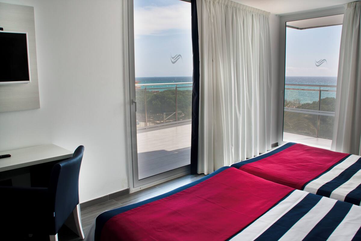 Une chambre d’hôtel avec un lit, un bureau et une vue sur l’océan, visible à travers une grande fenêtre.