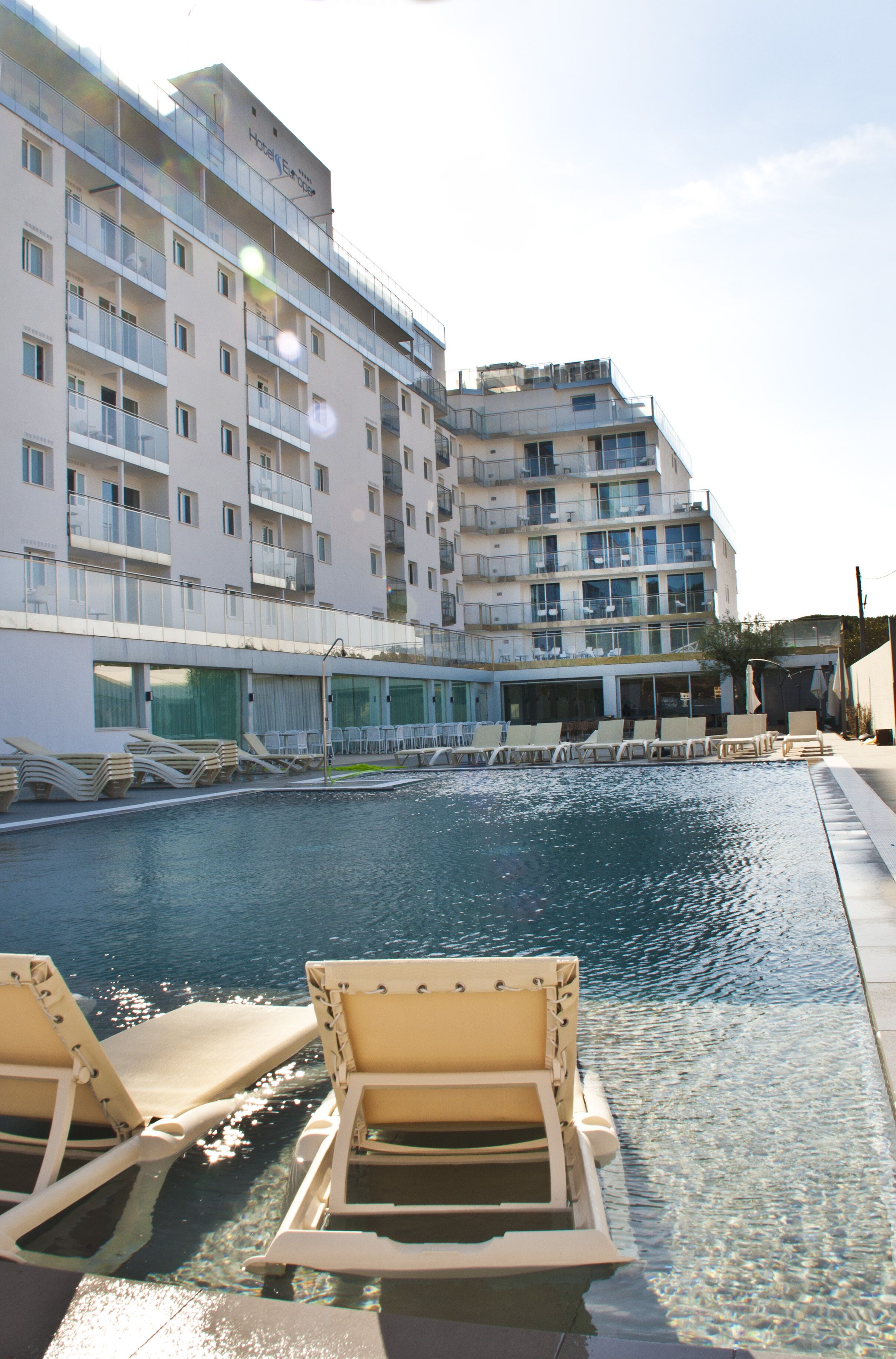 Un área de piscina de hotel con sillones reclinables y un edificio con varios balcones.
