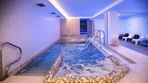 Ein Whirlpool mit gefliesten Stufen und Metallgeländern, umgeben von weißen Wänden und einem gefliesten Boden.