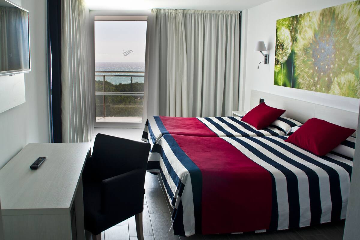 Ein Hotelzimmer mit einem Bett, einem Schreibtisch, einem Sessel und einem großen Fenster mit Vorhängen.