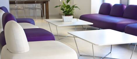 Un espace détente moderne avec des sièges blancs et violets, une table basse blanche et une plante en pot.