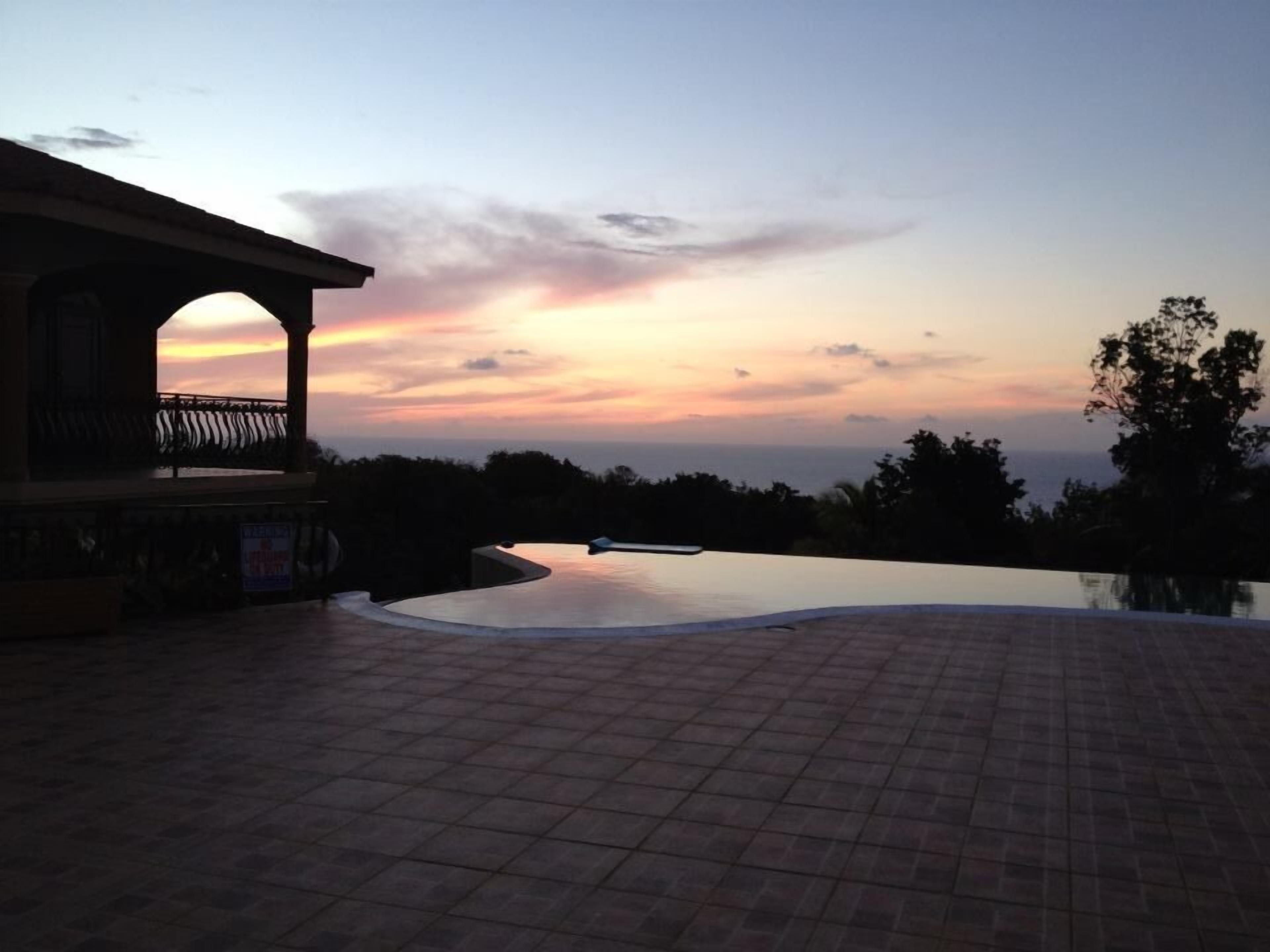 A sunset view from a tiled patio area with a pool.