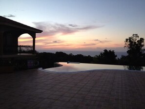 A sunset view from a tiled patio area with a pool.