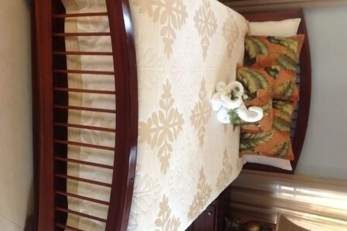 A room with a wooden bed, a patterned bedspread, and a decorative pillow.