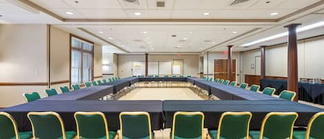 A conference room with a long table and green chairs, wooden flooring, and a ceiling with recessed lighting.