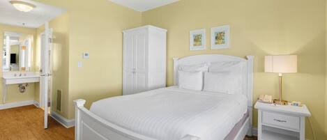 Een slaapkamer met een bed, nachtkastje, dressoir en een badkamer met wastafel en spiegel.