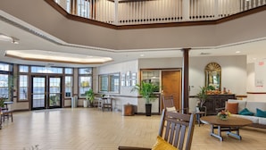 A spacious lobby with a high ceiling, large windows, and a central seating area with a round table and chairs. - Oakwood Resort (Syracuse)