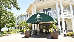 The entrance of Oakwood Resort with a covered porch, large potted plants, and a view of Lake Wawasee. - Oakwood Resort (Syracuse)