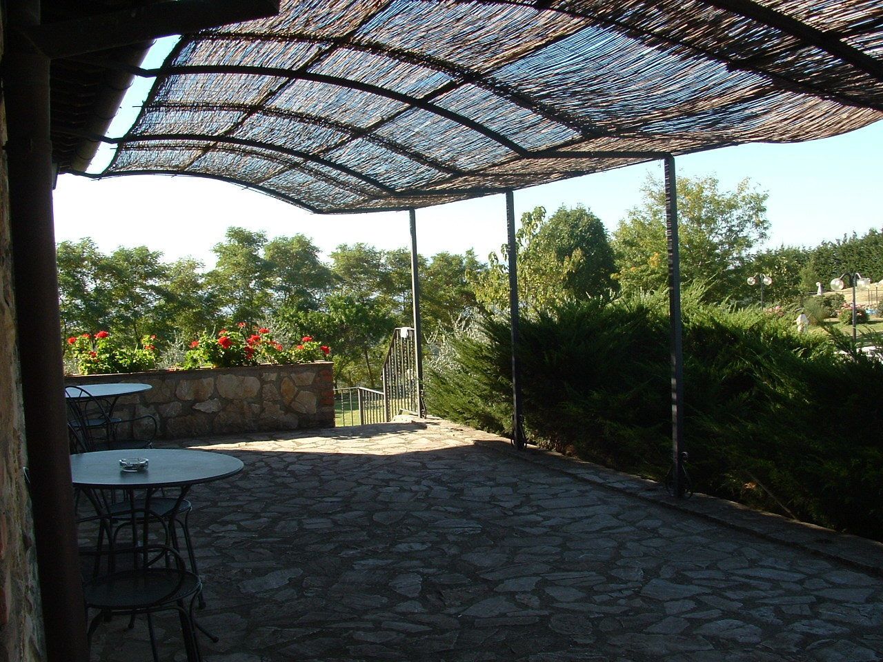 An outdoor patio with stone flooring, metal chairs, and a woven shade structure.