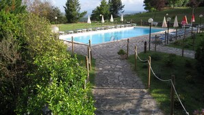 Una piscina rodeada de sillas de descanso y sombrillas, con un camino de piedra que la conduce.