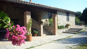 Un edificio de piedra con techo de tejas, una chimenea de ladrillo y una pequeña escalera que lleva a la entrada. Hay plantas y flores en macetas cerca de la entrada.