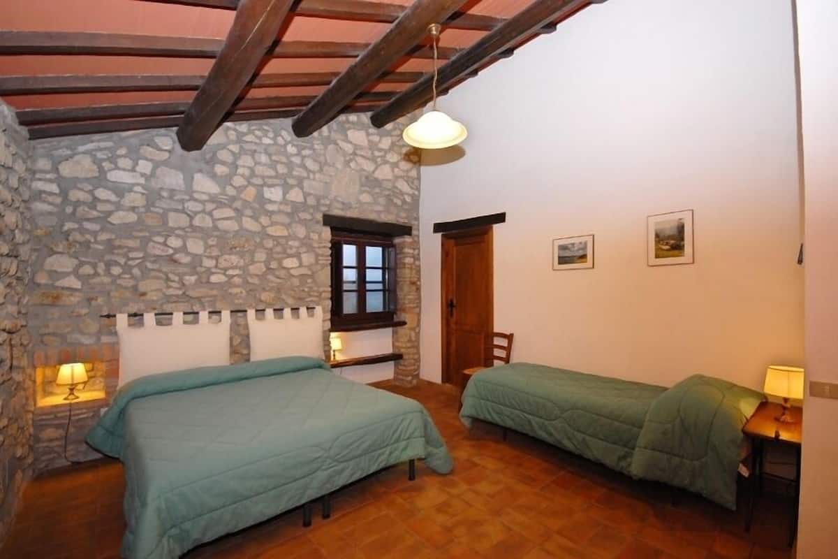 Una habitación con dos camas, paredes de piedra, vigas de madera, una ventana y una puerta.