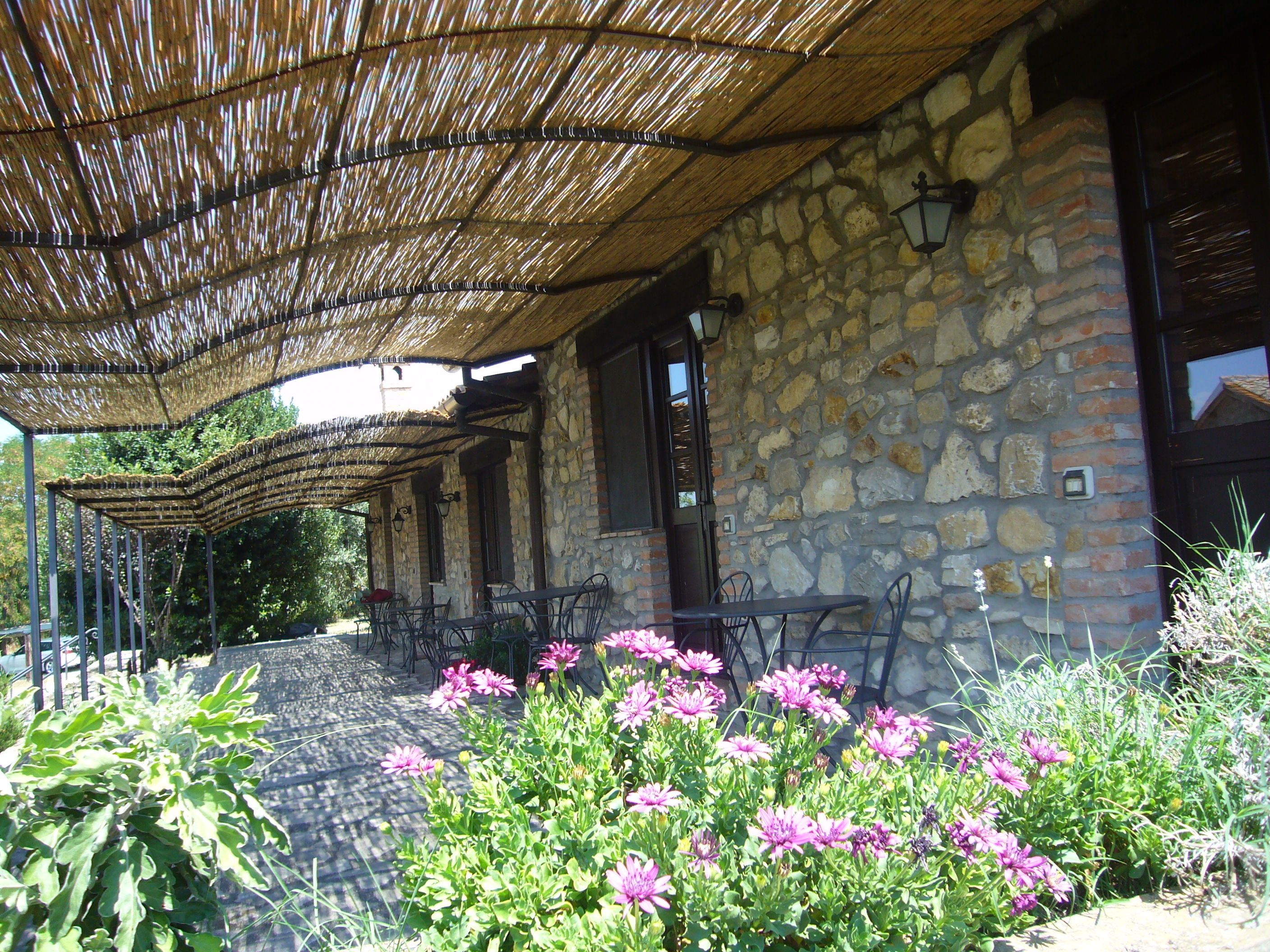 A stone building with a thatched roof patio area, outdoor seating, and flowering plants.