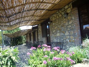 Edificio de piedra con techo de paja, zona de patio, asientos exteriores y plantas con flores.