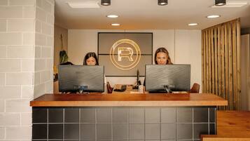 A reception desk with two computer monitors, a logo on the wall, and a wooden panel on the right.