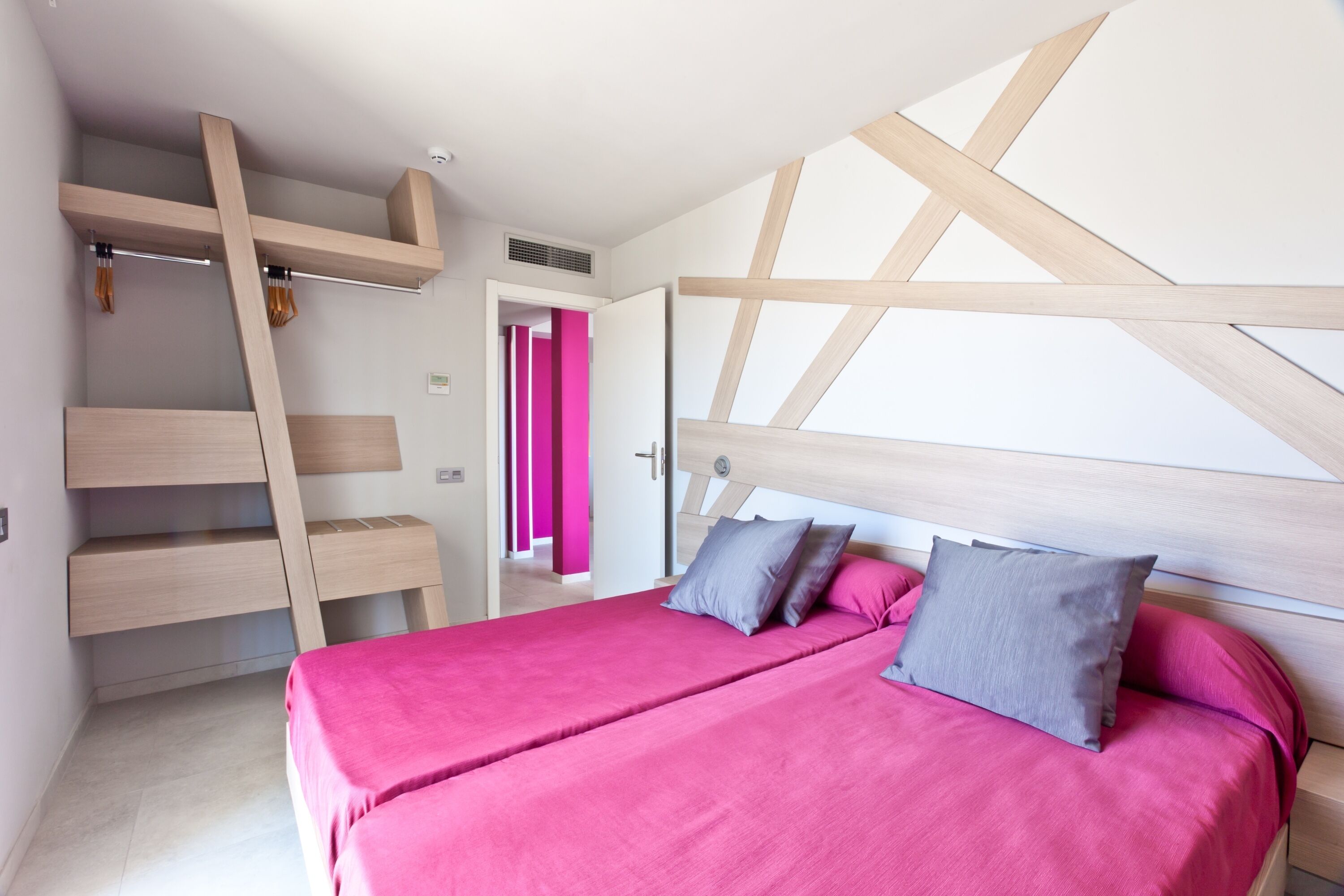 A modern bedroom with a bed, two pillows, a staircase, and a bright pink door.