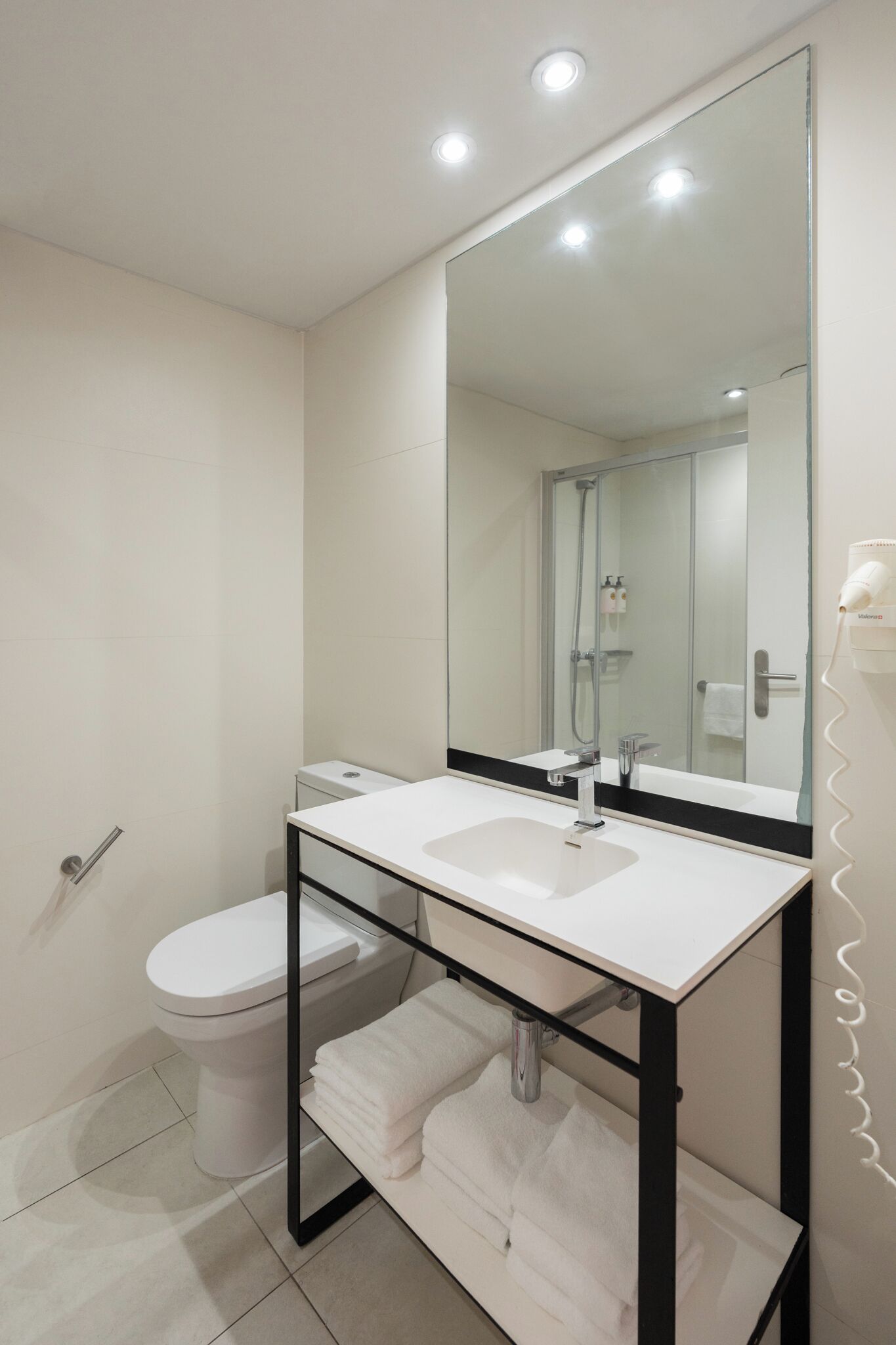 Une salle de bain moderne avec un lavabo blanc, un grand miroir et une douche à parois de verre.