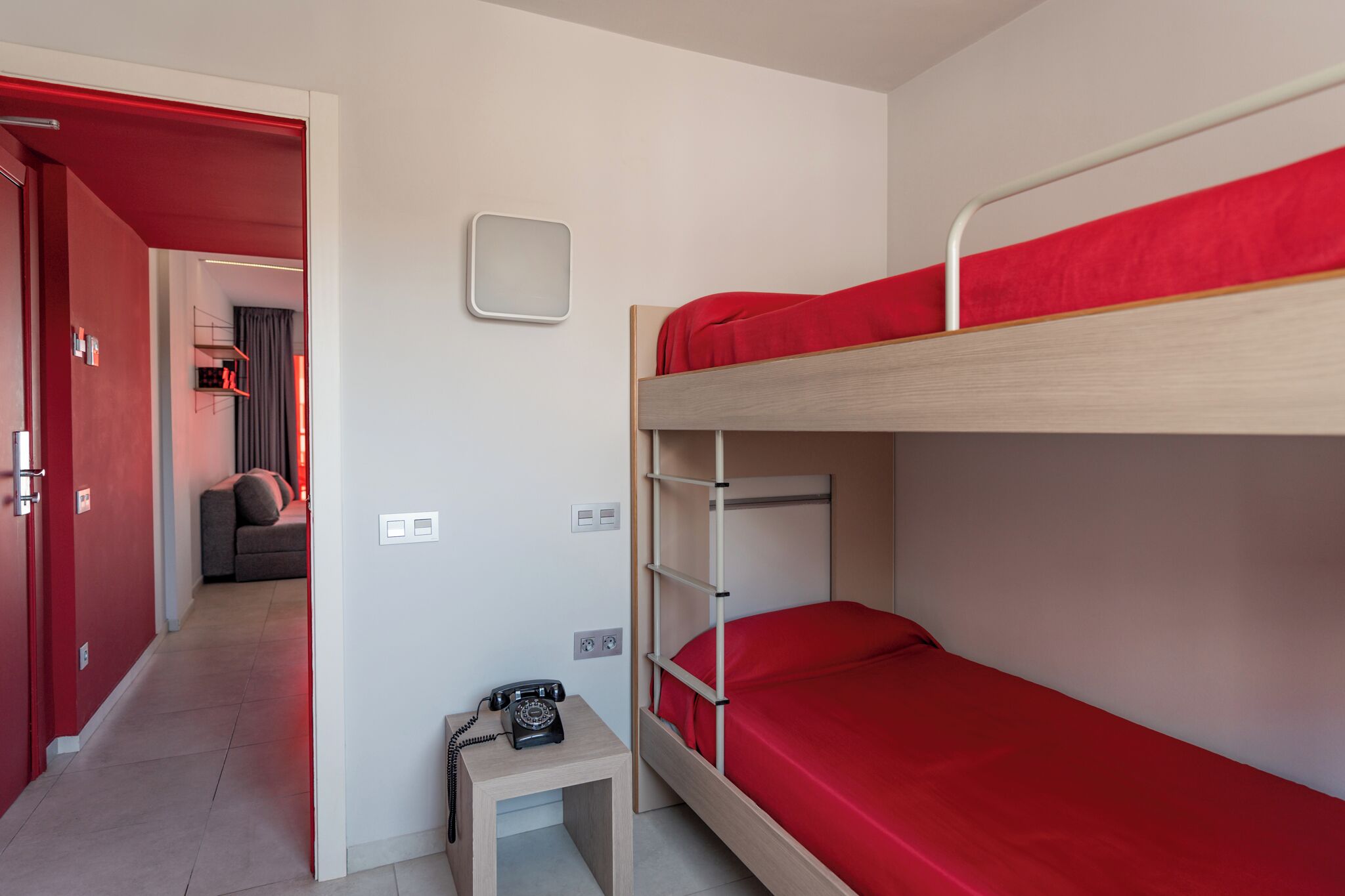 Camera con letto a castello, un materasso rosso, un comodino con il telefono e un piccolo sgabello.
