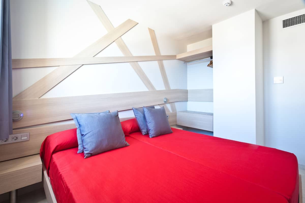 Un dormitorio moderno con colcha roja, cabecero de madera y un escritorio integrado con silla.
