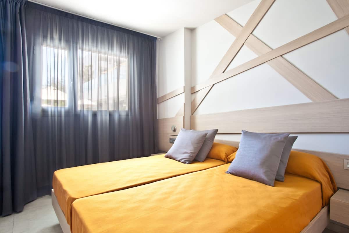 Una habitación de hotel con una cama doble, una mesita de noche, una lámpara y una ventana con cortinas.