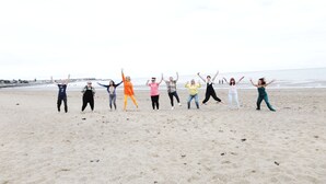 A group of people standing on a sandy beach with their arms raised, facing the ocean. - Bryn Woodlands House (Colwyn Bay)