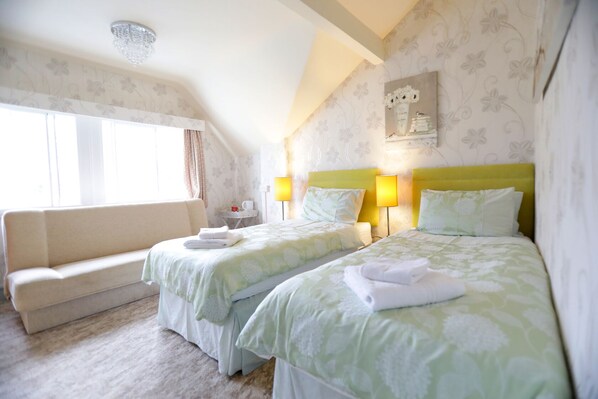 A hotel room with two beds, a sofa, a lamp, and a painting on the wall. - Bryn Woodlands House (Colwyn Bay)