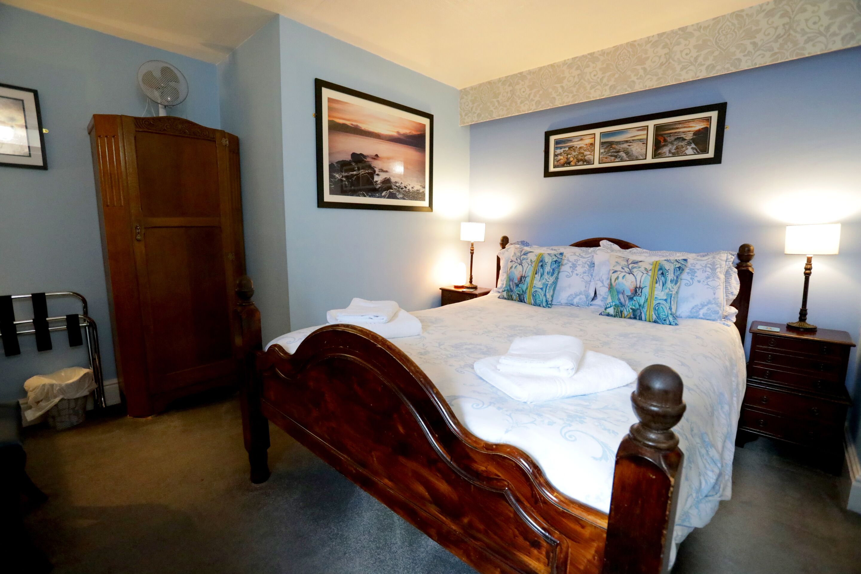 Un dormitorio ordenado con una cama de madera, una mesita de noche con lámparas, un armario y una pared decorada con cuadros.