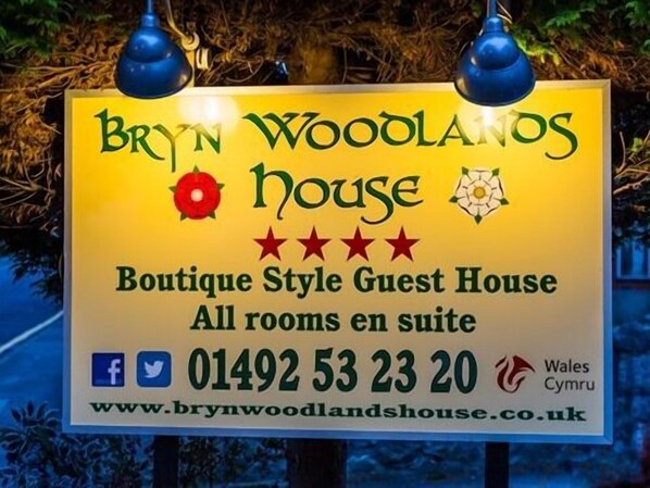 Señal de Bryn Woodland House, una casa de huéspedes de estilo boutique con todas las habitaciones tipo suite, número de contacto 01492 53 23 20 y sitio web www.brynwoodlandhouse.co.uk.