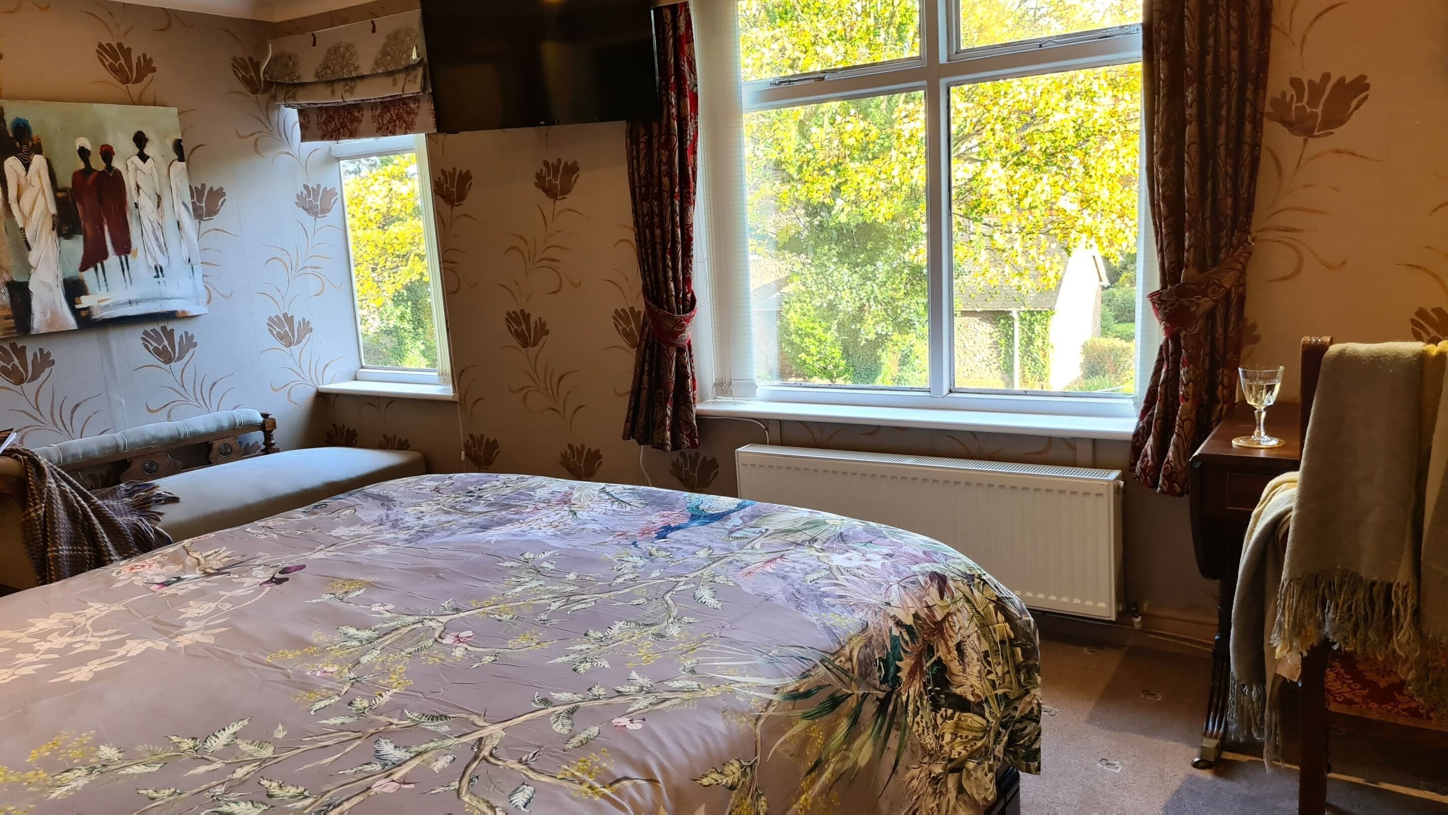 Une chambre avec un grand lit, une fenêtre avec des rideaux, un radiateur et un tableau au mur.