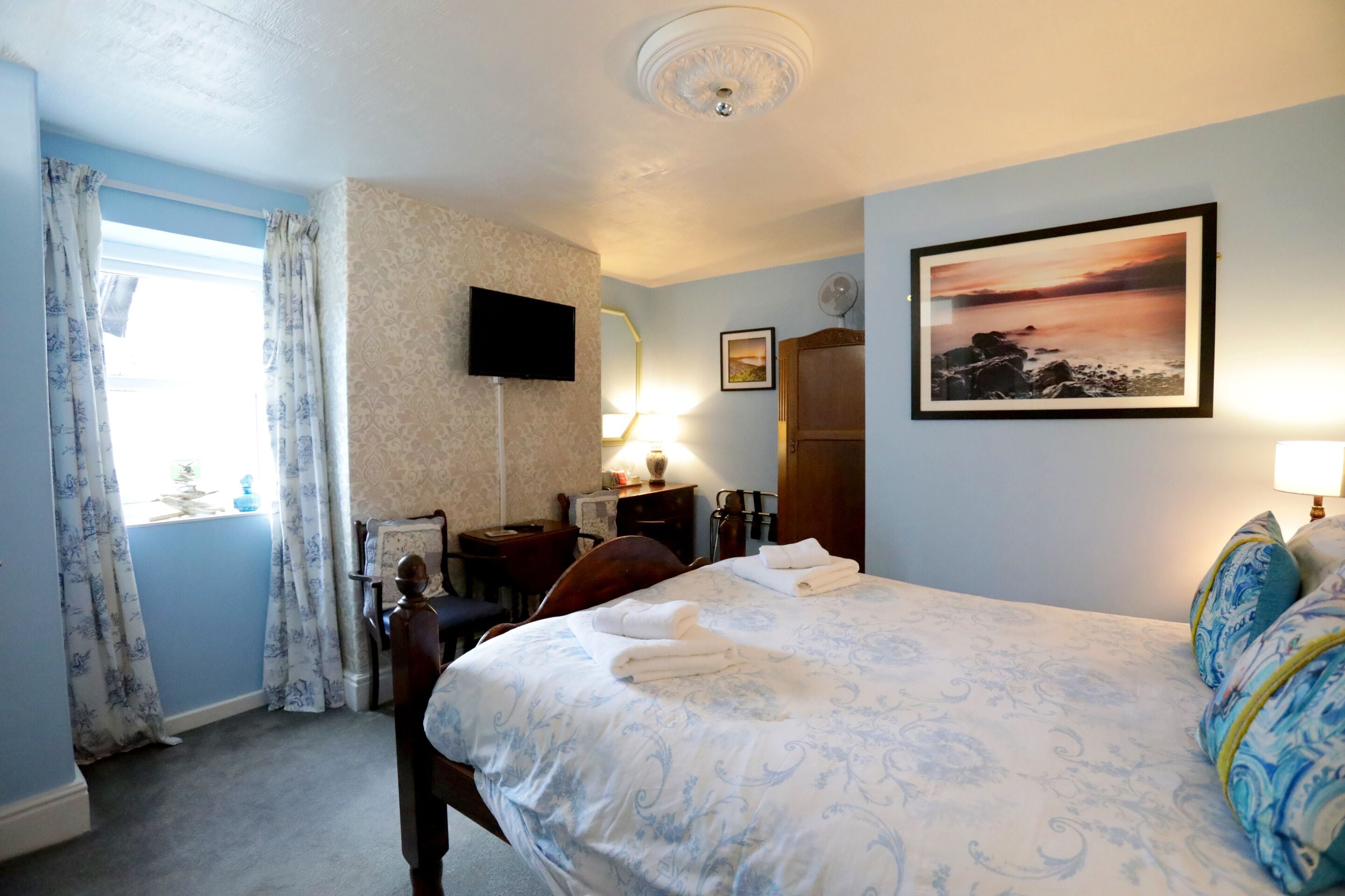 Une chambre d’hôtel avec un lit, un bureau, une chaise, une télévision et un tableau au mur.