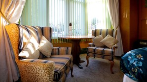 A room with striped upholstered chairs, a round wooden table, and a view through large windows with sheer curtains. - Bryn Woodlands House (Colwyn Bay)