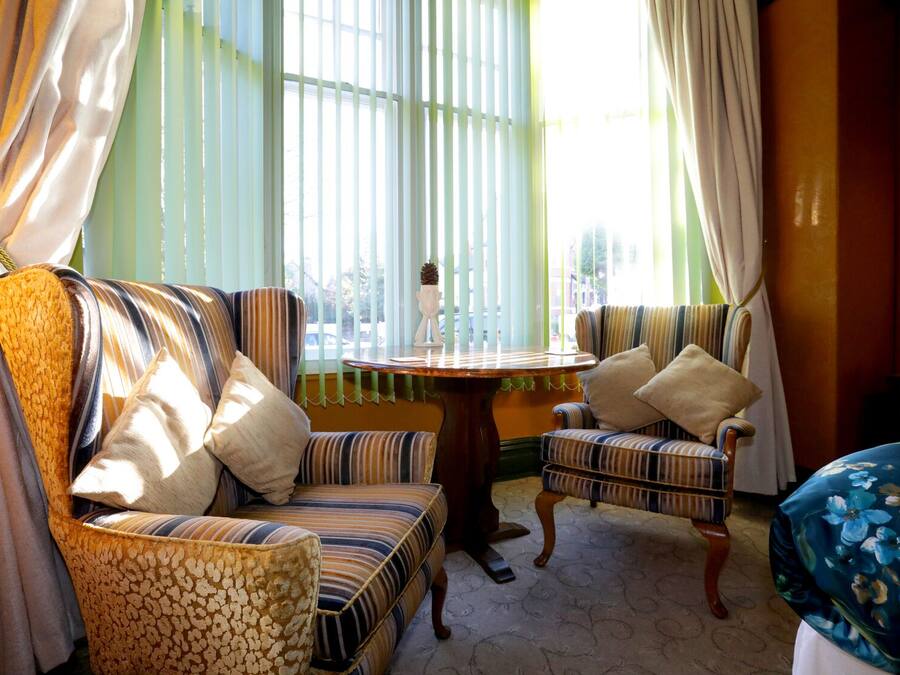 A room with striped upholstered chairs, a round wooden table, and a view through large windows with sheer curtains.