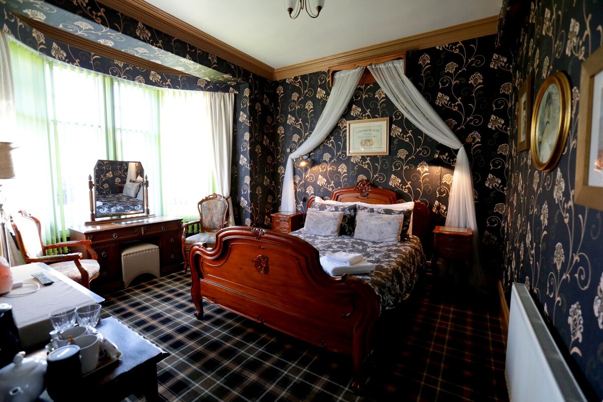 A traditional bedroom with a wooden bed, a desk with a chair, and a window with curtains.