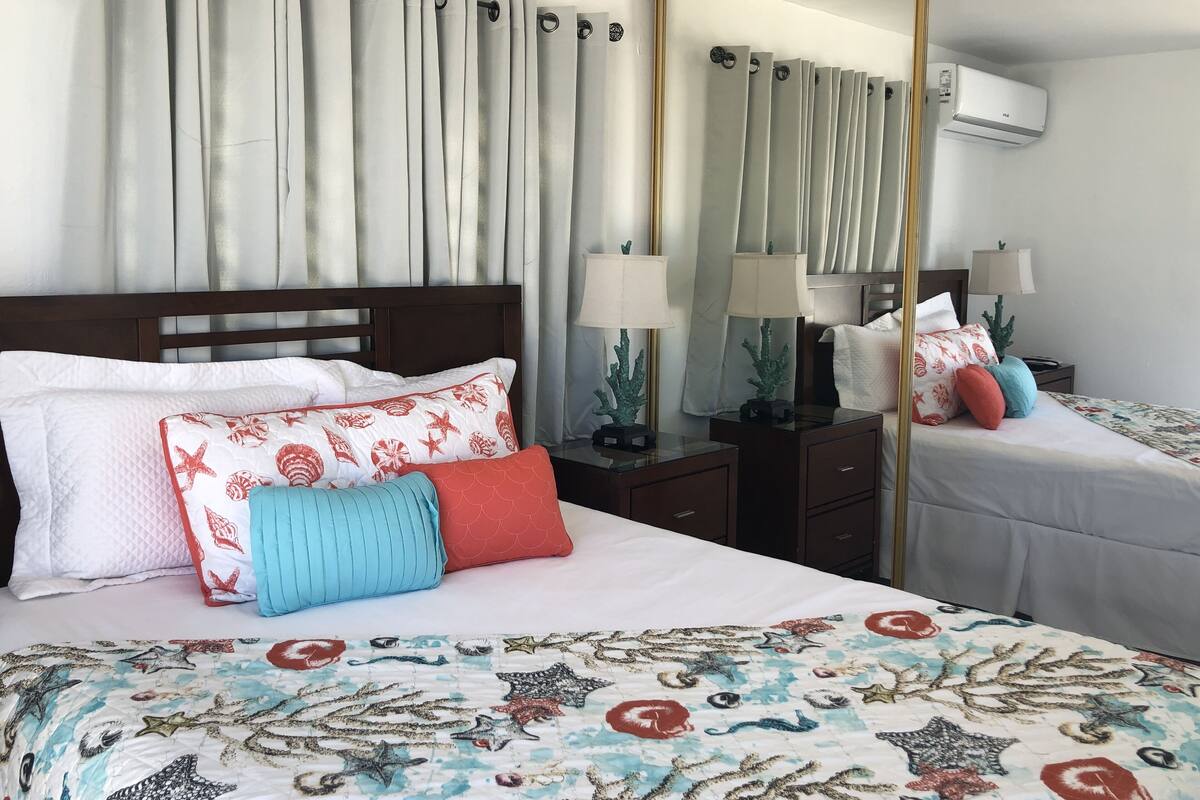A hotel room with a bed, two bedside tables with lamps, a nightstand, a mirror, and a window with curtains.