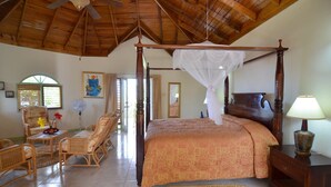 Una habitación amplia con cama con dosel, ventilador de techo, muebles de mimbre y vistas a través de una ventana.
