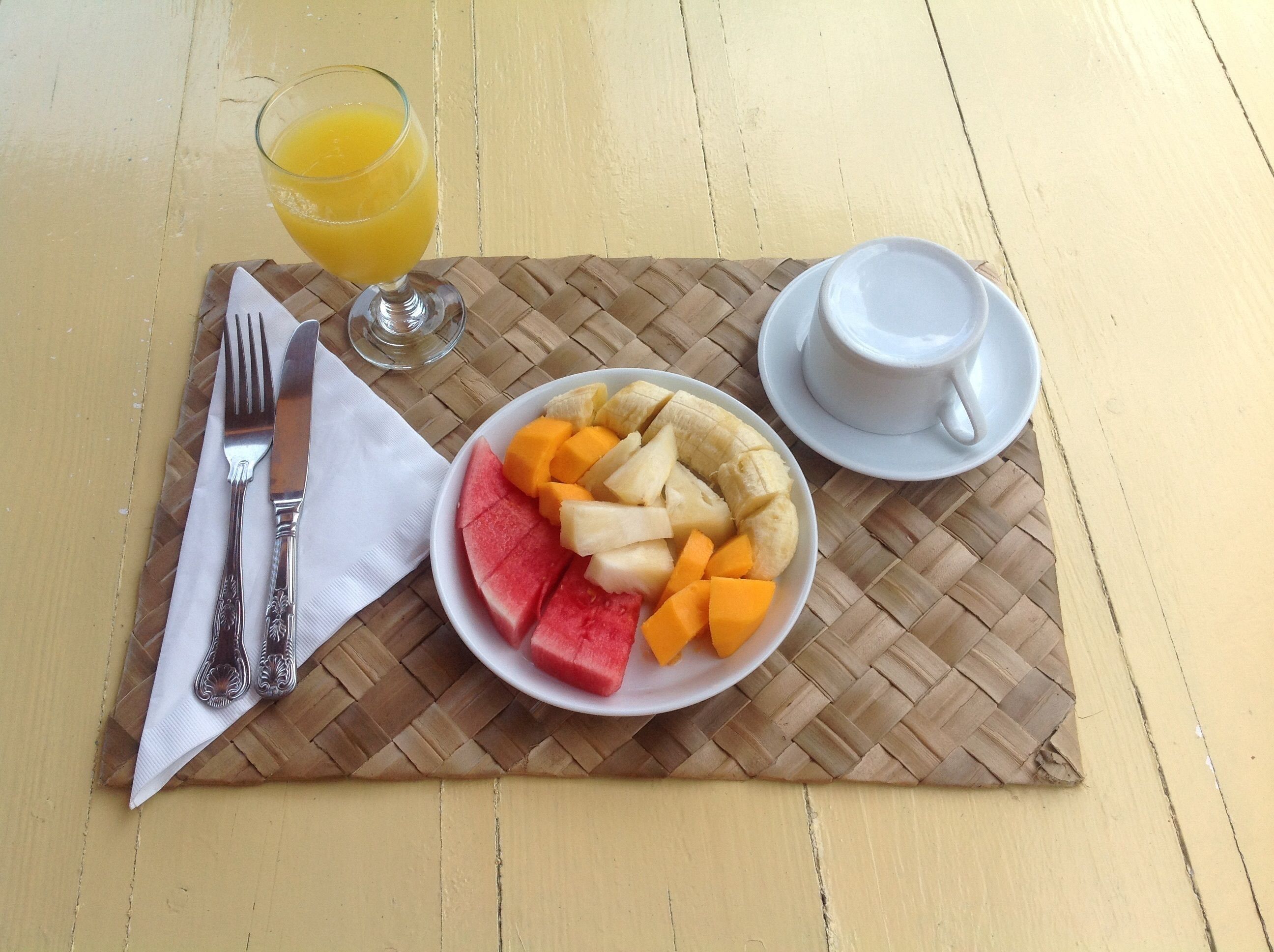 A meal with a plate of fruit, a glass of orange juice, and a cup of coffee on a woven placemat.