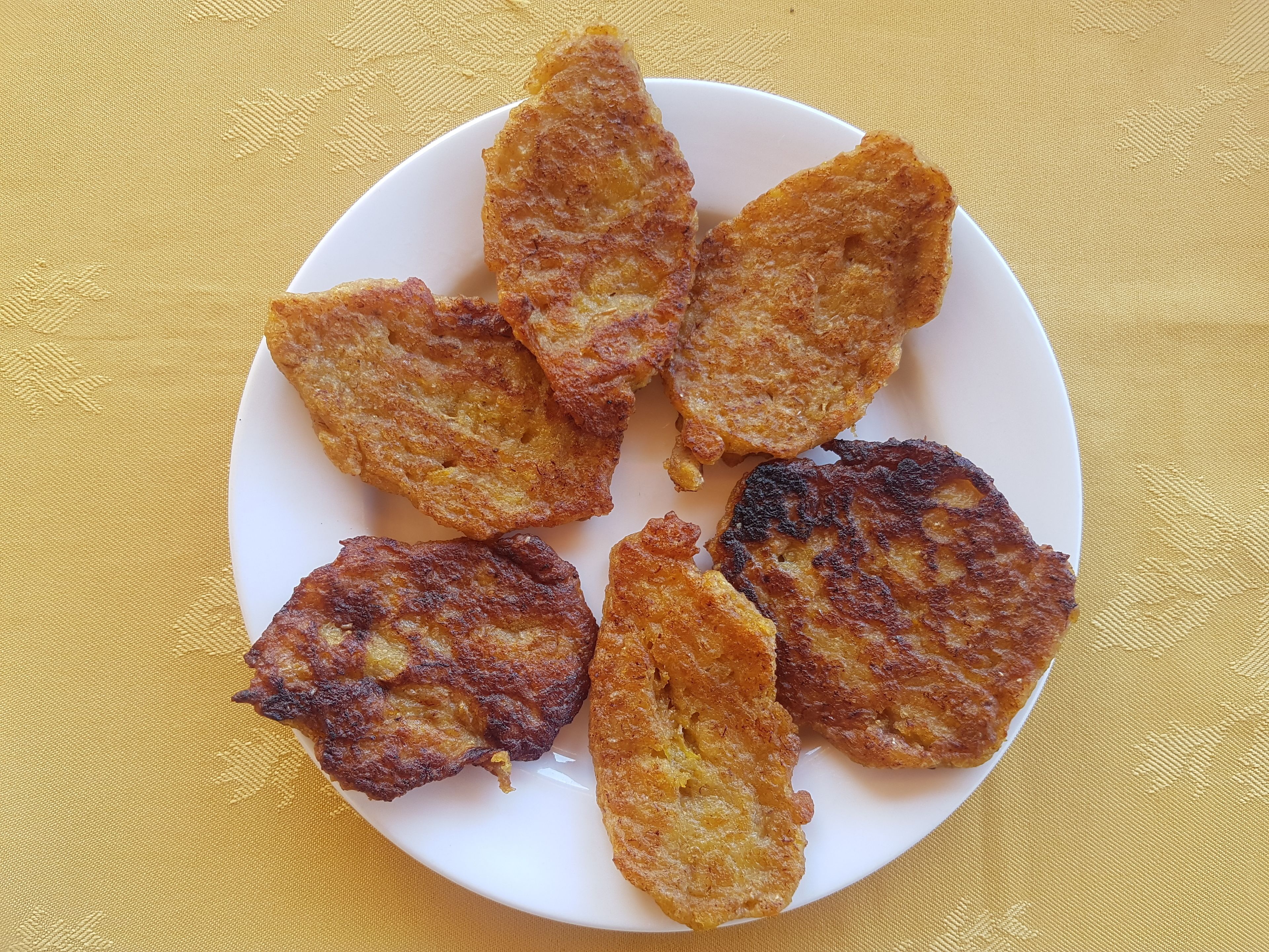 A white plate with six golden-brown fried items on a yellow textured tablecloth.